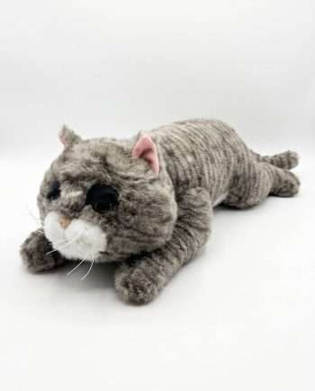 Gray plush cat stuffed toy lying on its stomach with pink ears and white muzzle against a white background, soft and cuddly.
