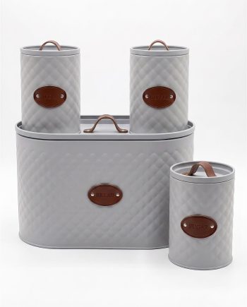 Light gray quilted metal canister set labeled TEA, COFFEE, BREAD, and SUGAR with brown leather tags on a white background.