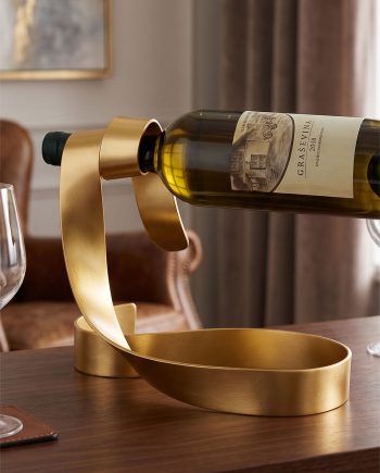Wine bottle placed in a gold metal holder on a wooden dining table, ready to pour or serve